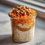 Close-up of carrot cake overnight oats in a jar, topped with shredded carrots and walnuts.