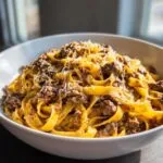 A close-up of a bowl of creamy Cheeseburger Alfredo Pasta topped with shredded cheese and seasoned ground beef.