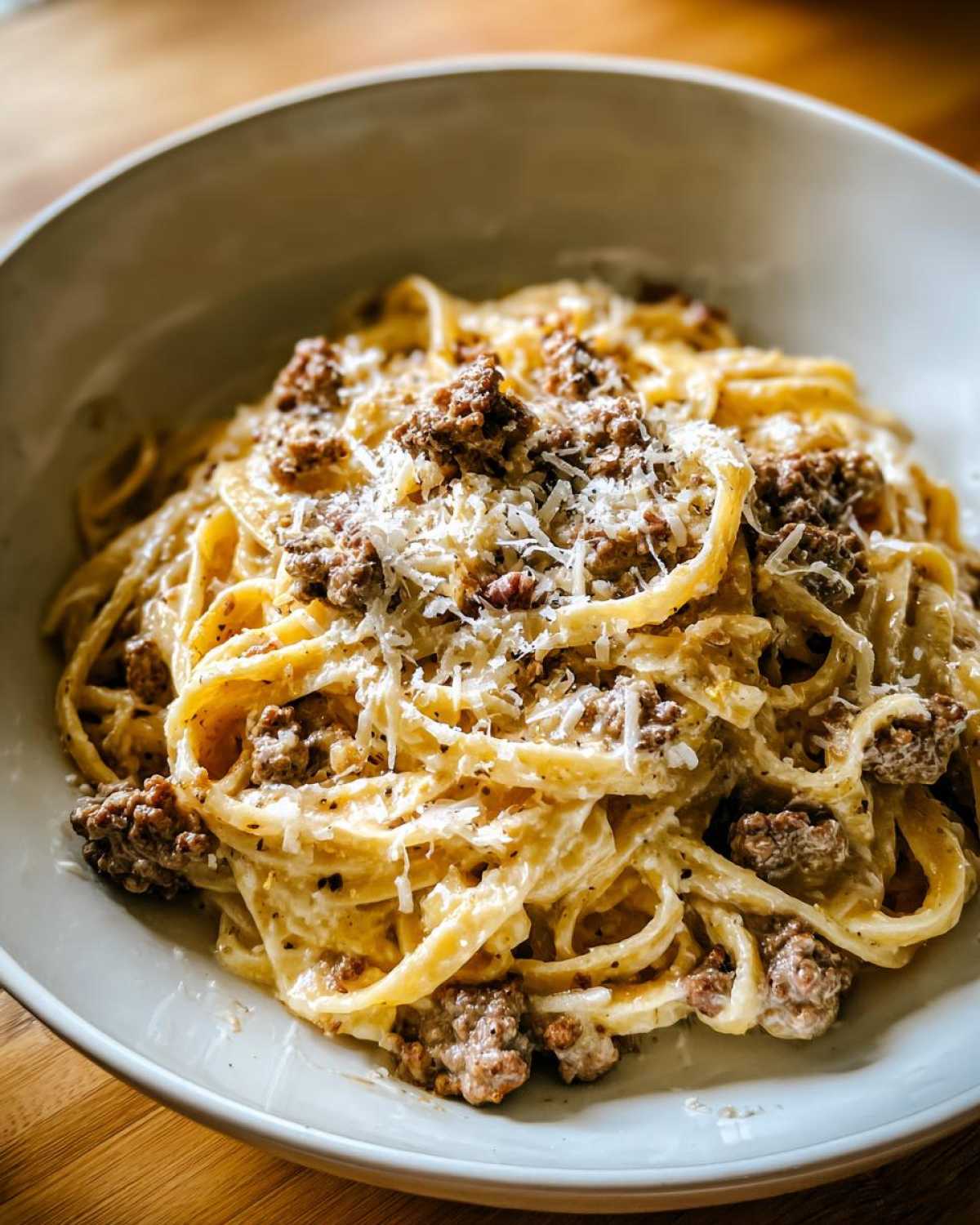 A close-up of creamy Cheeseburger Alfredo Pasta topped with crumbled ground beef and grated Parmesan cheese.