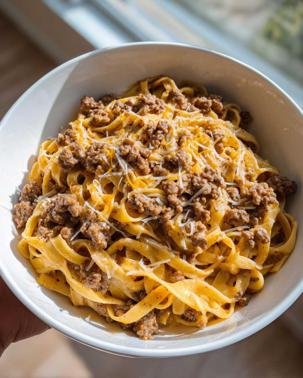A close-up of a bowl of creamy Cheeseburger Alfredo Pasta topped with seasoned ground beef and shredded cheese.