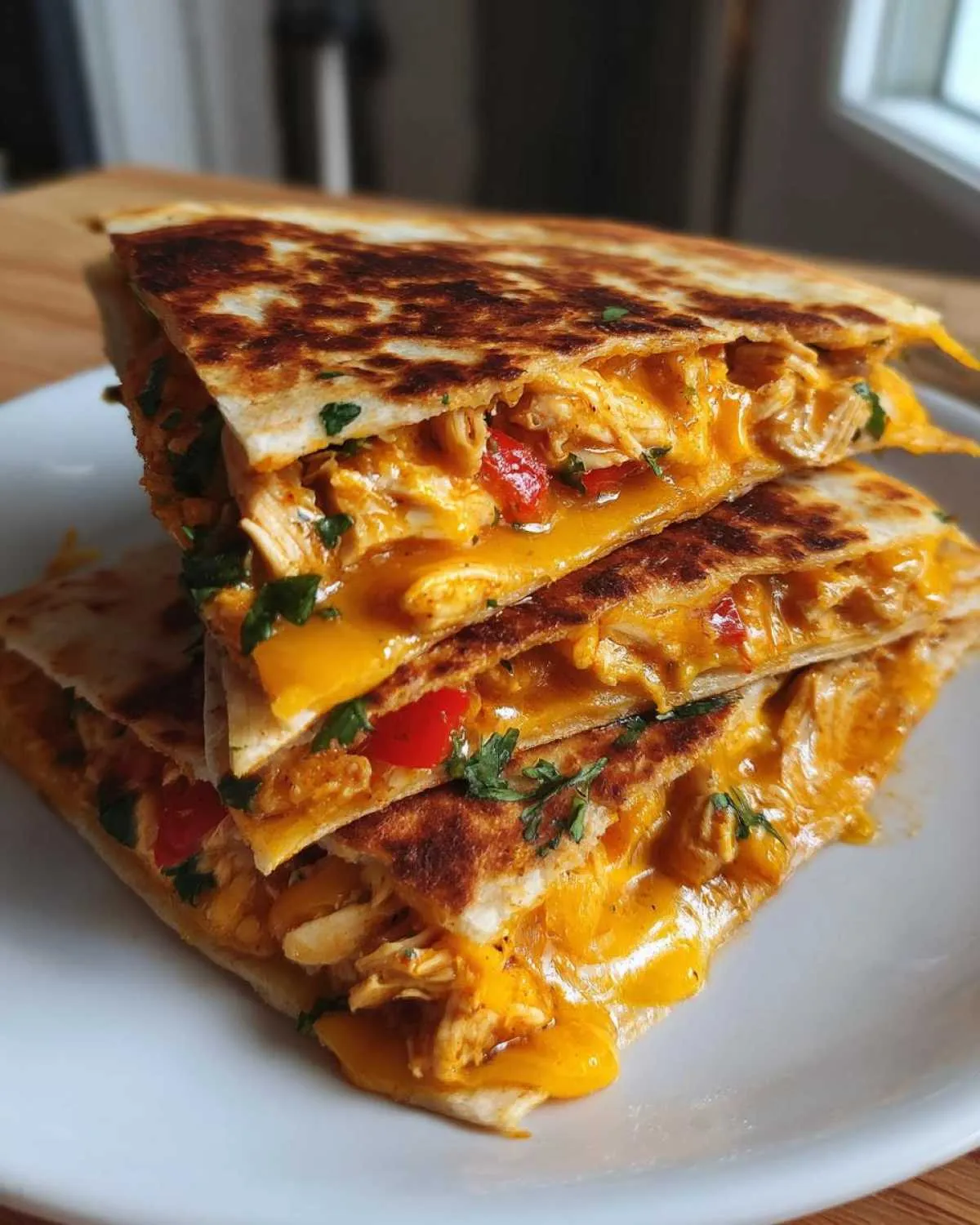A stack of three cheesy chicken quesadilla wedges, filled with shredded chicken, melted cheddar cheese, and red peppers, garnished with cilantro.