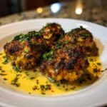 Close-up of four golden-brown chicken christopher bites in a buttery sauce, garnished with fresh parsley.