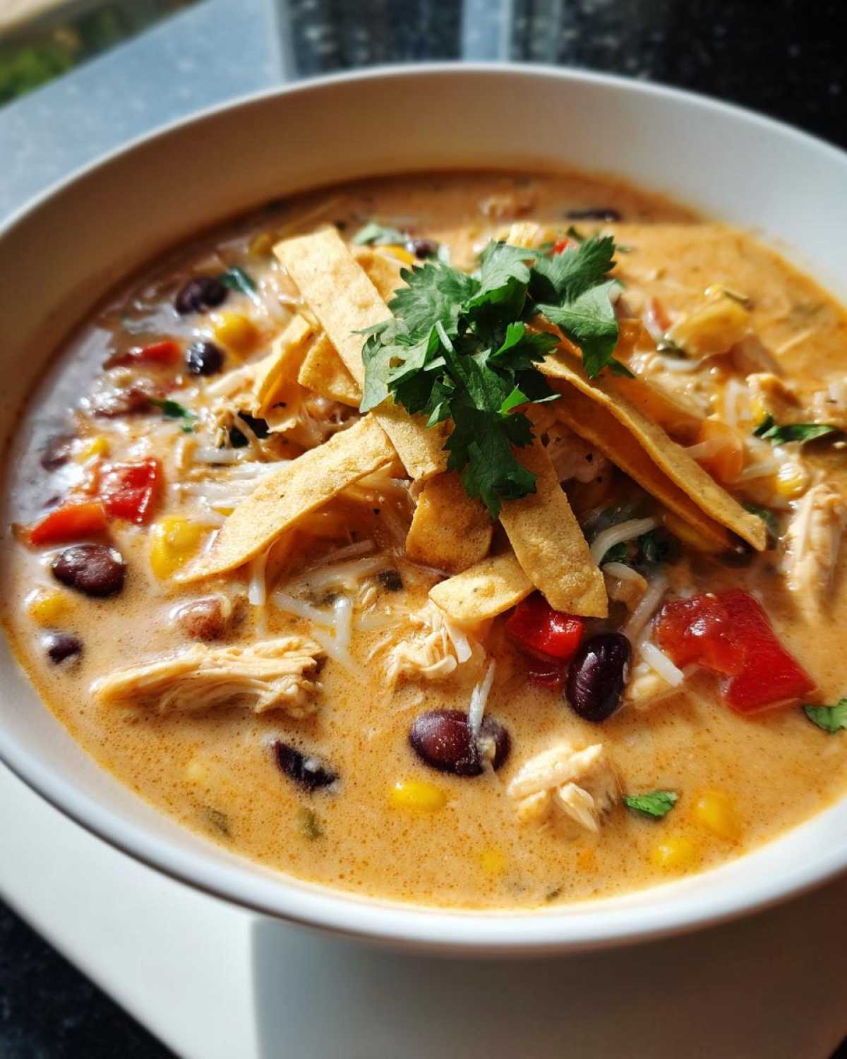 A bowl of creamy Chilis chicken enchilada soup topped with tortilla strips and cilantro.