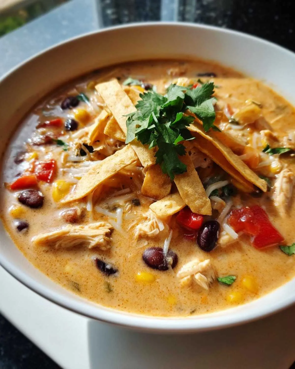 A close-up of a bowl of creamy Chilis chicken enchilada soup, topped with tortilla strips and cilantro.