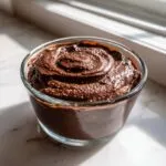 A close-up of creamy chocolate buttercream frosting swirled in a glass bowl, ready for decorating.
