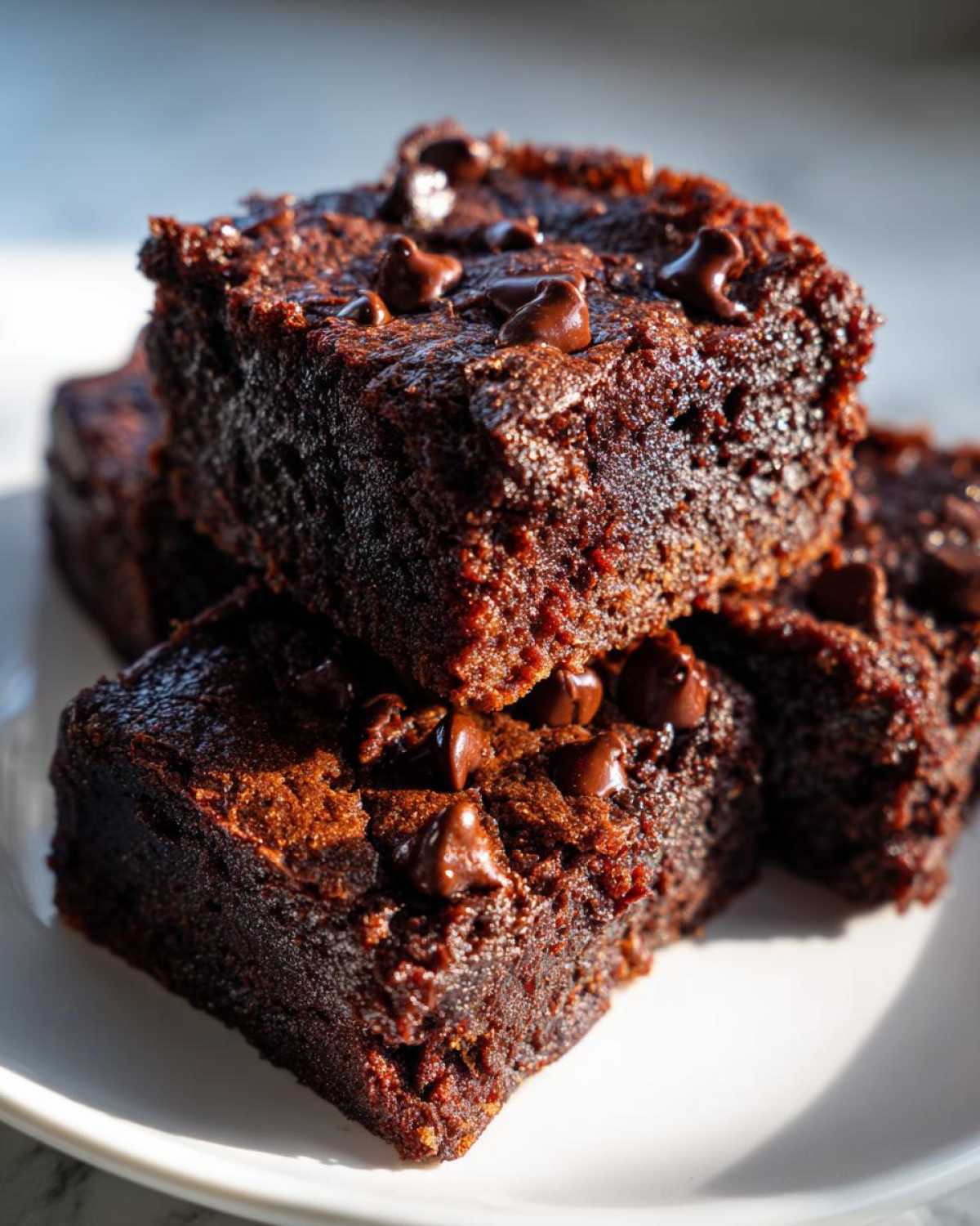 Close-up of stacked chocolate zucchini brownies topped with melted chocolate chips.
