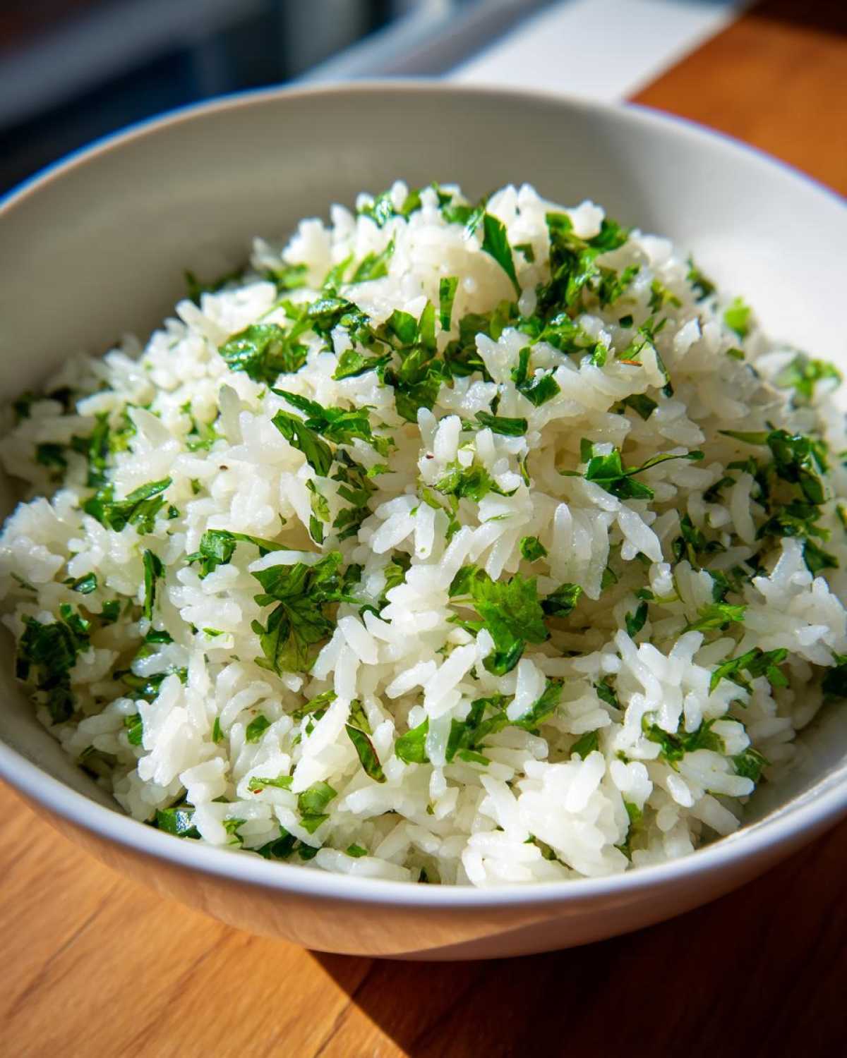 A close-up of fluffy white rice mixed with chopped fresh cilantro, served in a white bowl.