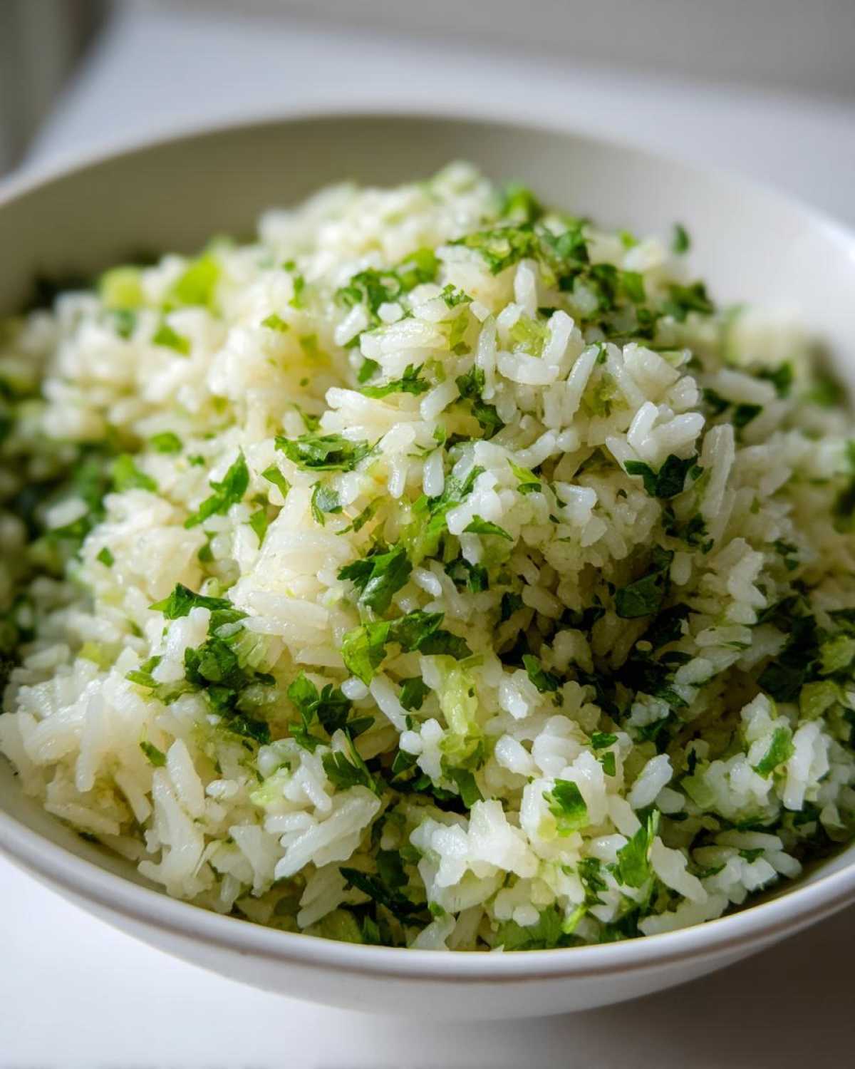 A close-up of fluffy cilantro lime rice in a white bowl, topped with fresh chopped cilantro and lime zest.