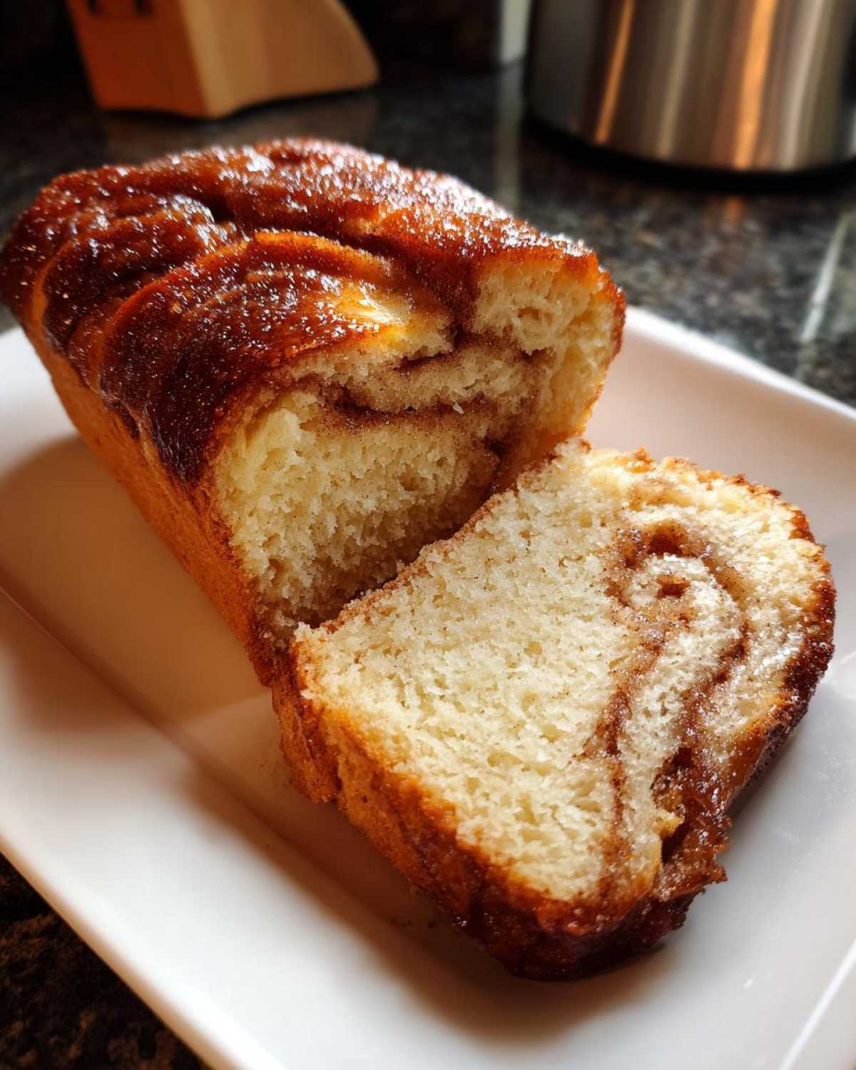 Close-up of a freshly baked cinnamon sugar bread loaf with a slice cut, showing the swirled cinnamon filling.