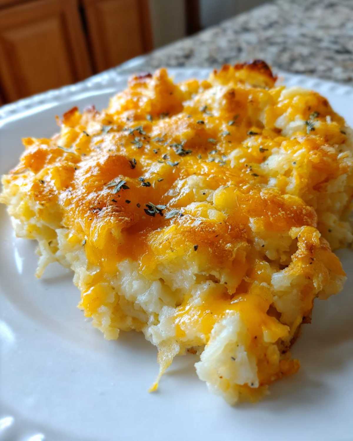 A close-up of a serving of Copycat Cracker Barrel hashbrown casserole, topped with melted cheddar cheese and sprinkled with herbs.