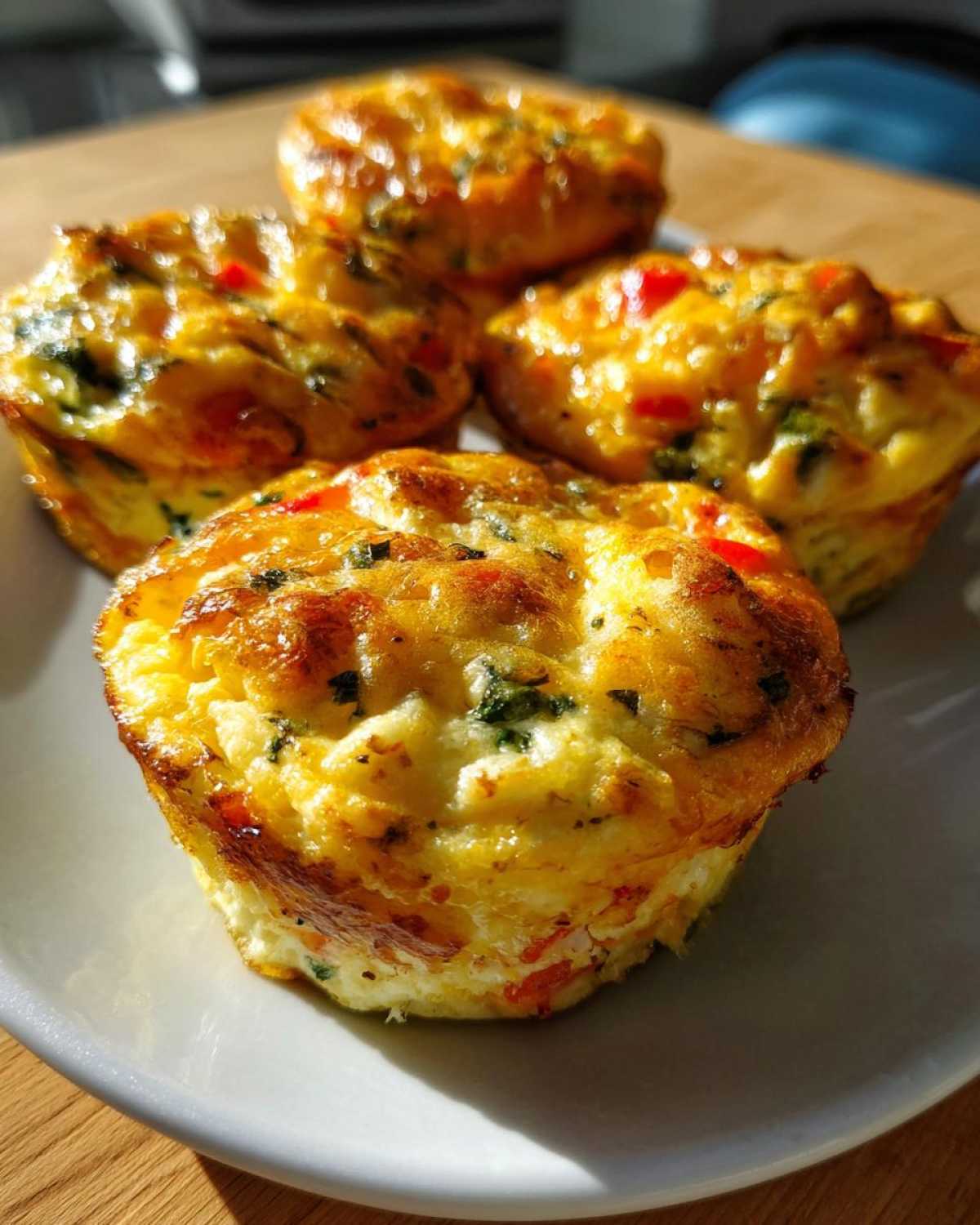 Close-up of fluffy cottage cheese egg bites with red bell peppers and green herbs on a white plate.