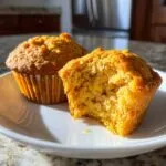 Close-up of two cottage cheese pumpkin muffins on a white plate, one with a bite taken out.