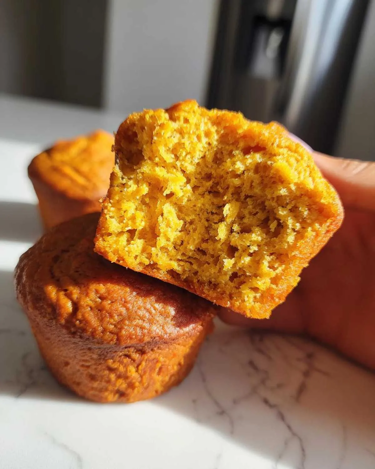 A close-up of a broken cottage cheese pumpkin muffin, revealing its fluffy texture and vibrant orange color.