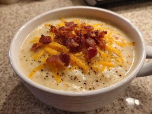 Close-up of a bowl of creamy crack potato soup topped with crispy bacon bits and shredded cheddar cheese.