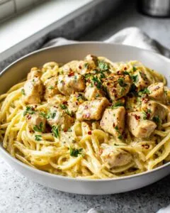A close-up of a bowl filled with creamy garlic parmesan chicken pasta, topped with parsley and red pepper flakes.