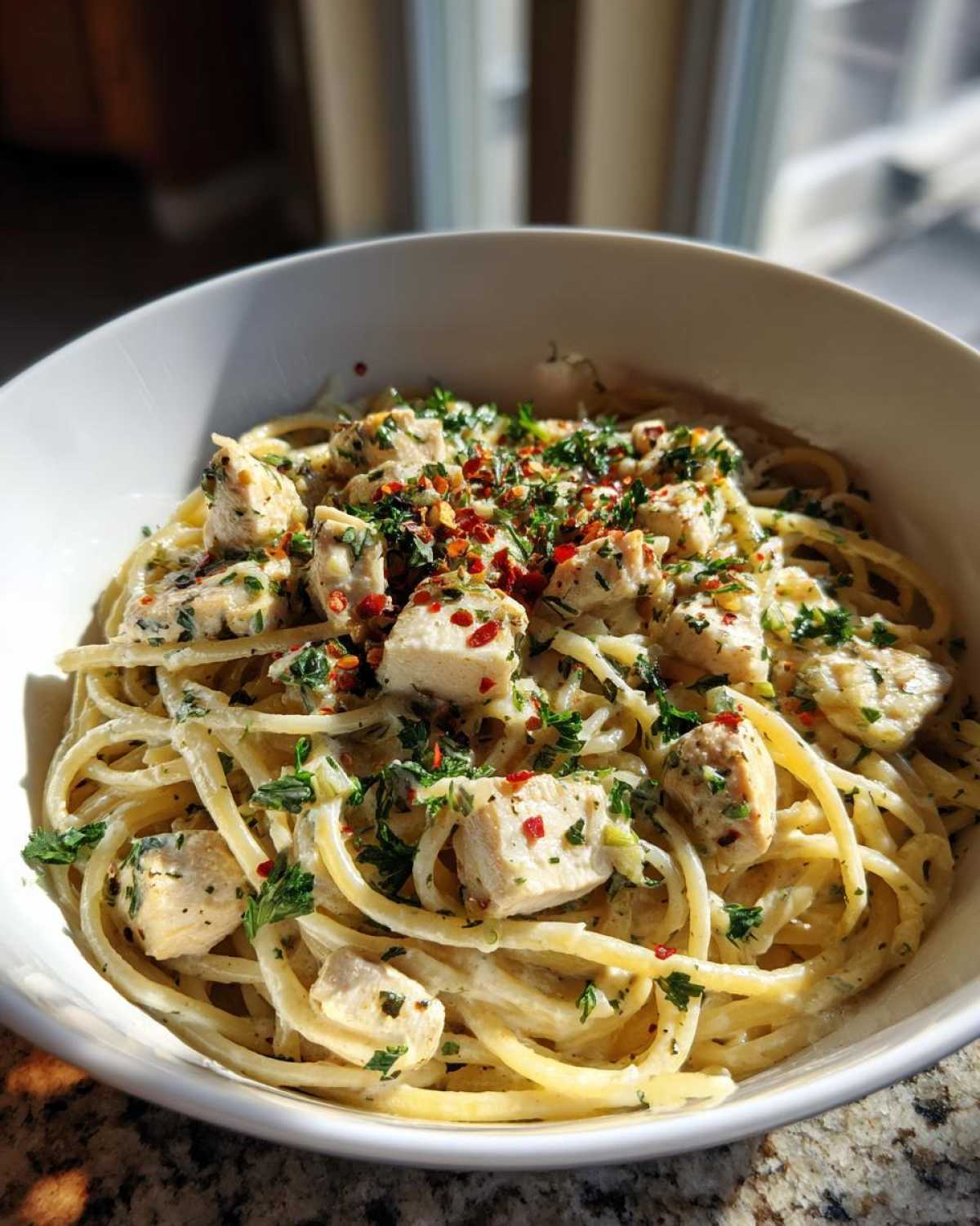 A bowl of creamy garlic parmesan chicken pasta topped with parsley and red pepper flakes.