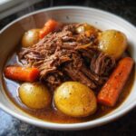 Close-up of a bowl filled with tender crock pot pot roast, potatoes, and carrots in savory gravy.