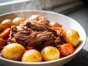 A steaming bowl of tender crock pot pot roast with whole potatoes and chunks of carrots.