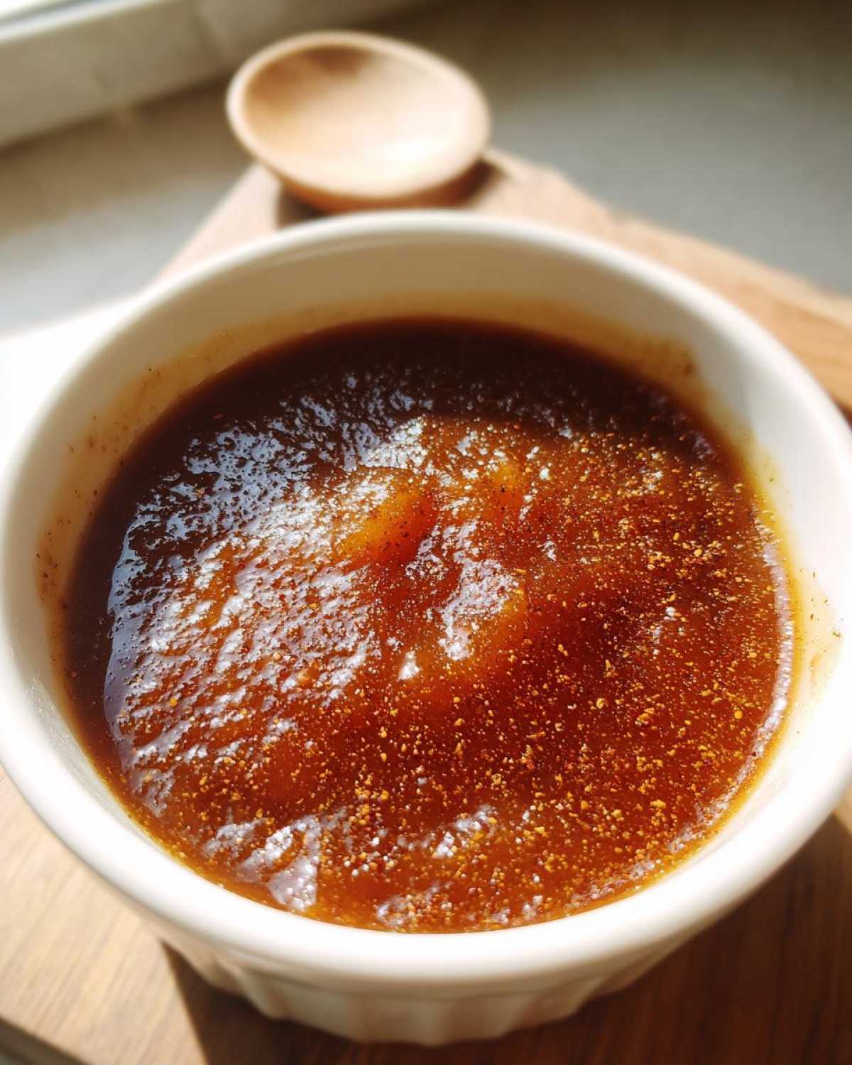 Close-up of rich, dark crockpot apple butter in a white bowl, sprinkled with cinnamon.