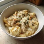 A bowl of creamy crockpot chicken alfredo tortellini, topped with melted cheese and parsley.