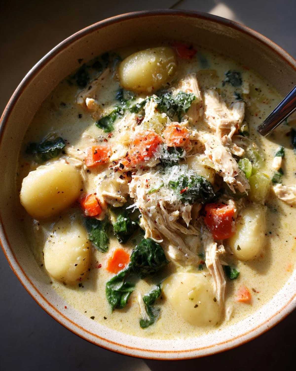 A close-up of a bowl of creamy crockpot chicken gnocchi soup, filled with tender chicken, soft gnocchi, spinach, and carrots.
