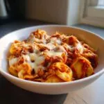 A bowl of delicious crockpot chicken tortellini topped with melted mozzarella cheese.