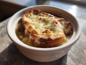 A close-up of a bowl of Crockpot French Onion Soup topped with a crusty bread slice and melted, browned cheese.