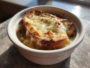 A close-up of a bowl of Crockpot French Onion Soup topped with a crusty bread slice and melted, browned cheese.