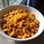 A bowl of easy beef goulash with macaroni pasta, seasoned ground beef, tomato sauce, and topped with melted cheddar cheese.