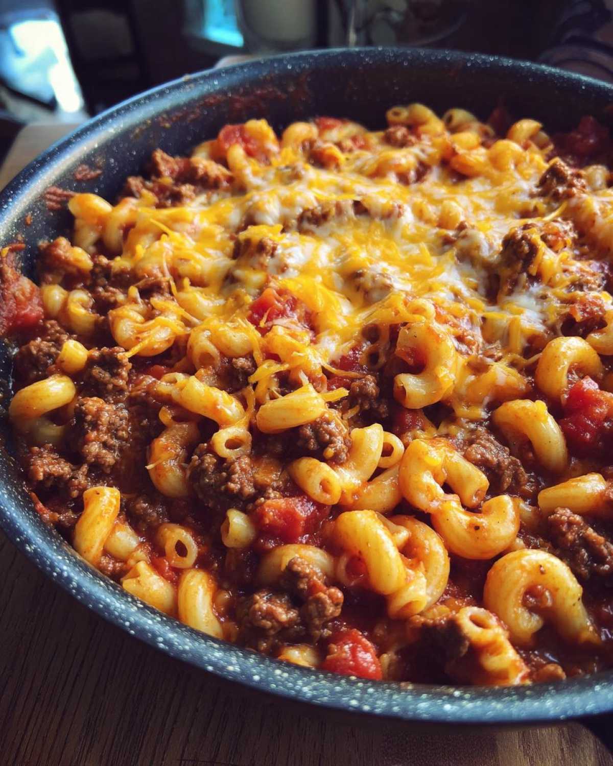 Close-up of a skillet filled with easy beef goulash, featuring elbow macaroni, ground beef, tomato sauce, and melted cheddar cheese.