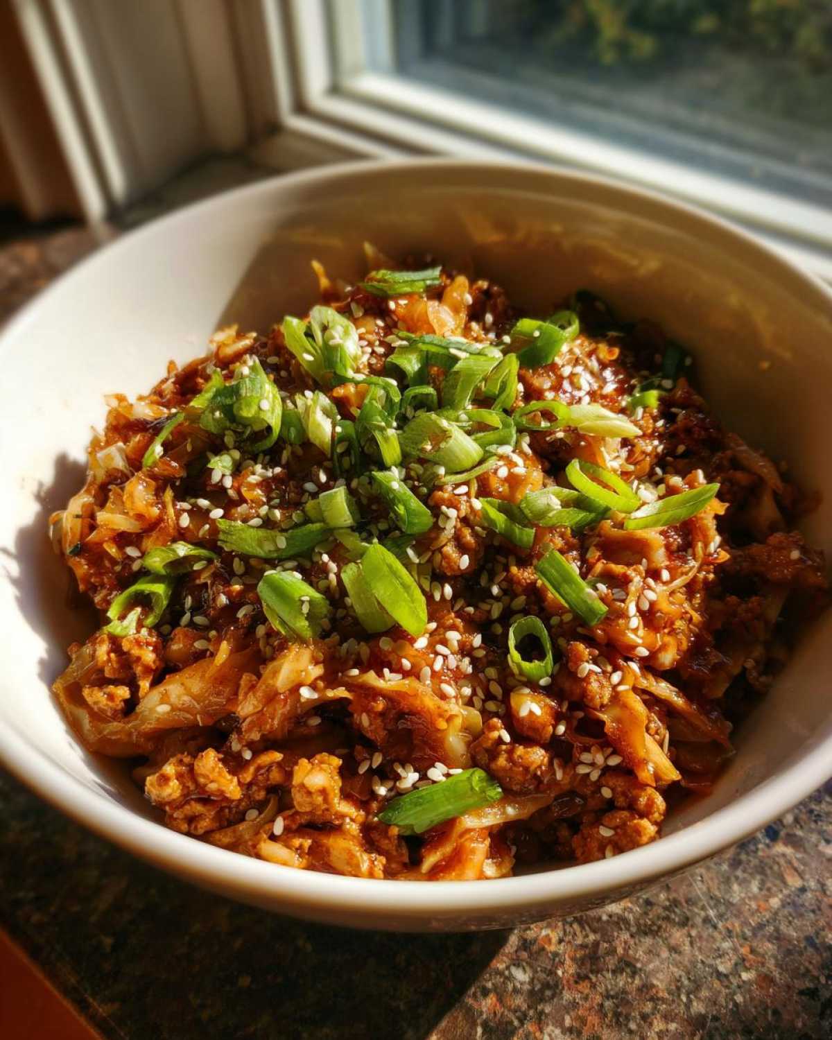 A close-up of a white bowl filled with a savory Egg Roll in a Bowl, topped with chopped green onions and sesame seeds.