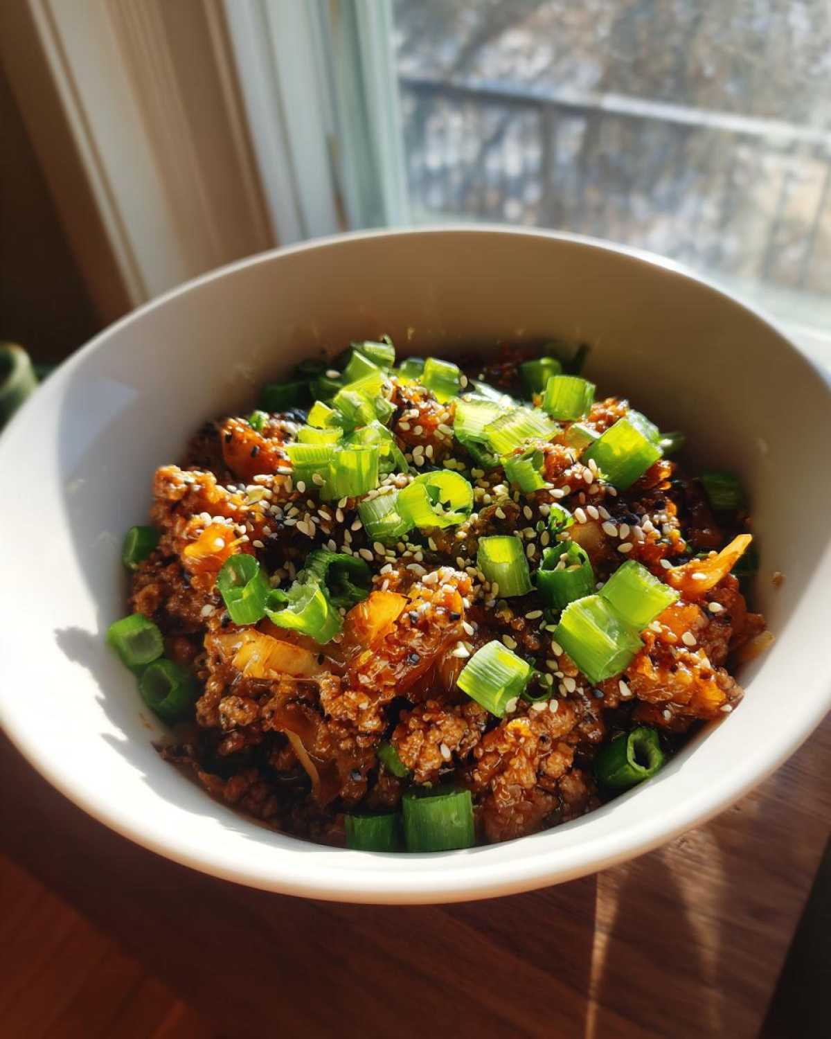 A close-up of a white bowl filled with a savory Egg Roll in a Bowl, topped with chopped green onions and sesame seeds.