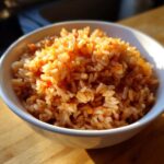 Close-up of fluffy Spanish rice in a white bowl, seasoned with red spices.