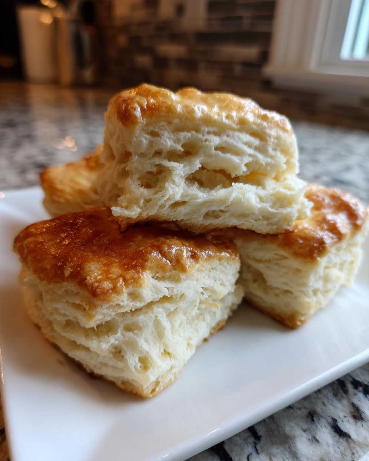 Close-up of golden-brown, fluffy tea biscuits stacked on a white plate, showcasing their flaky layers.