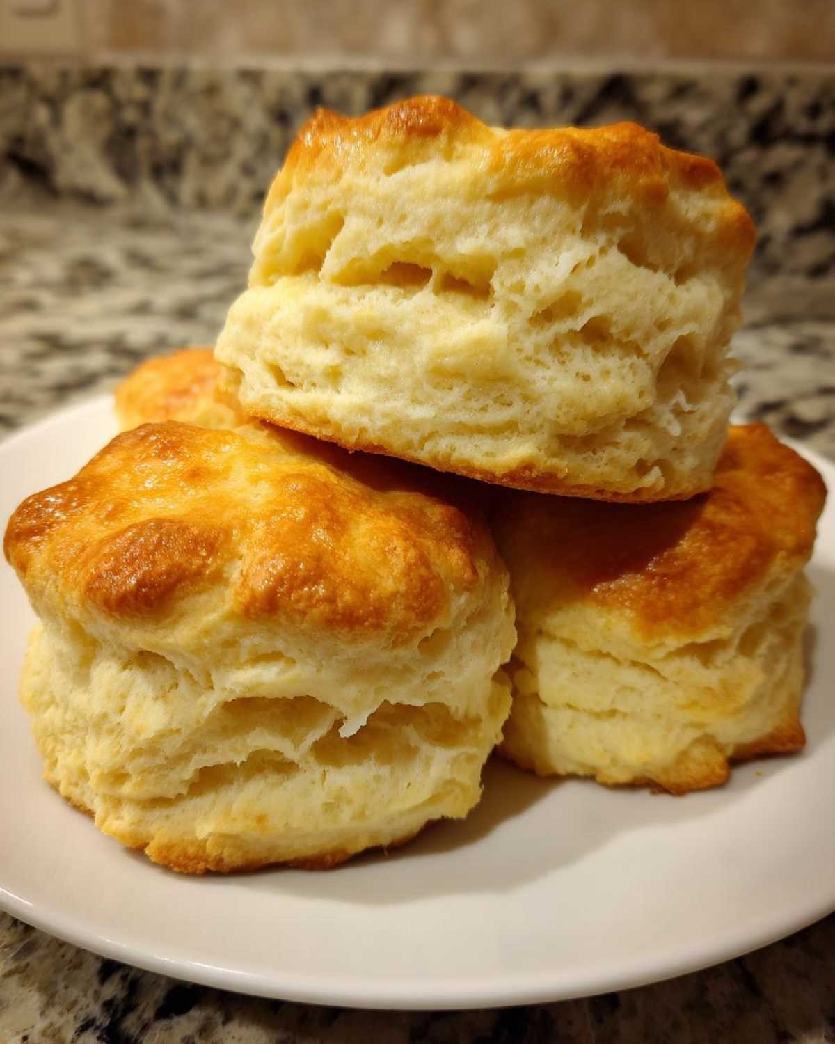 A close-up of a stack of golden-brown fluffy tea biscuits on a white plate.