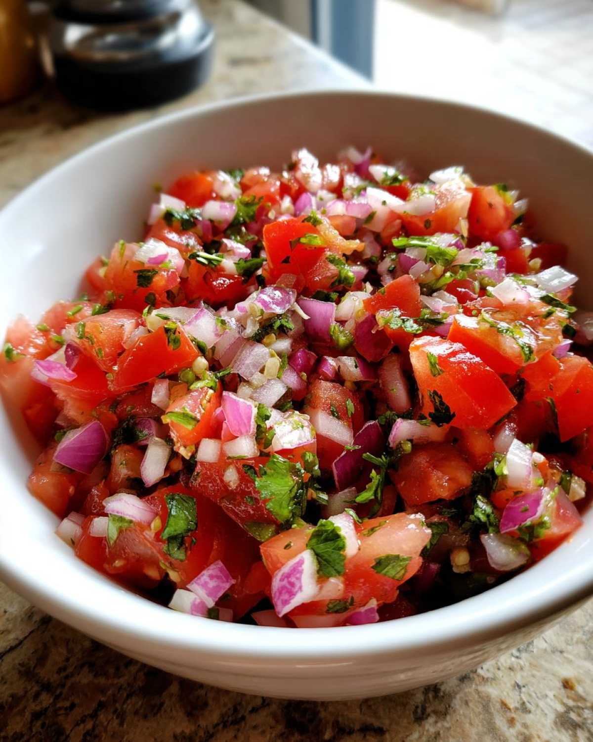 Close-up of a white bowl filled with fresh pico de gallo salsa, featuring diced tomatoes, red onion, cilantro, and jalapeño.