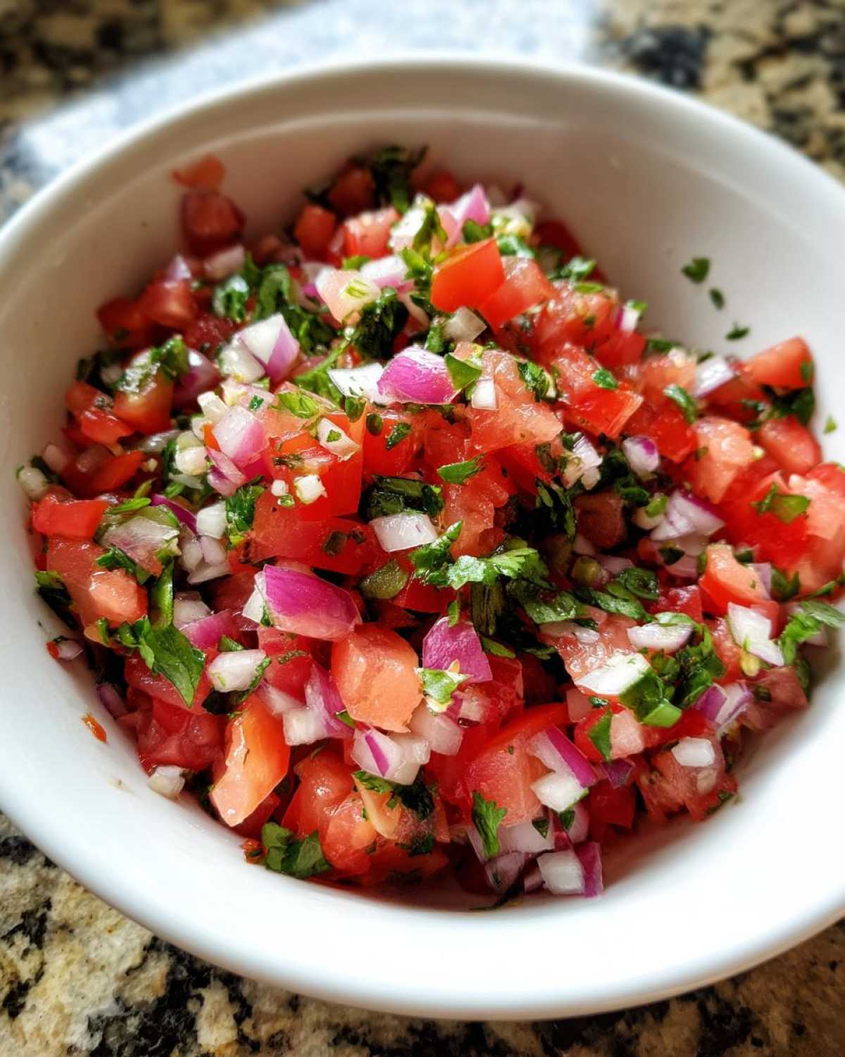 Close-up of a bowl filled with fresh, vibrant salsa made with chopped tomatoes, red onion, and cilantro.
