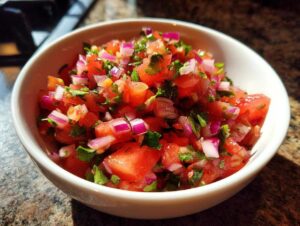 Close-up of a white bowl filled with fresh, vibrant salsa, featuring chopped tomatoes, red onion, and cilantro.
