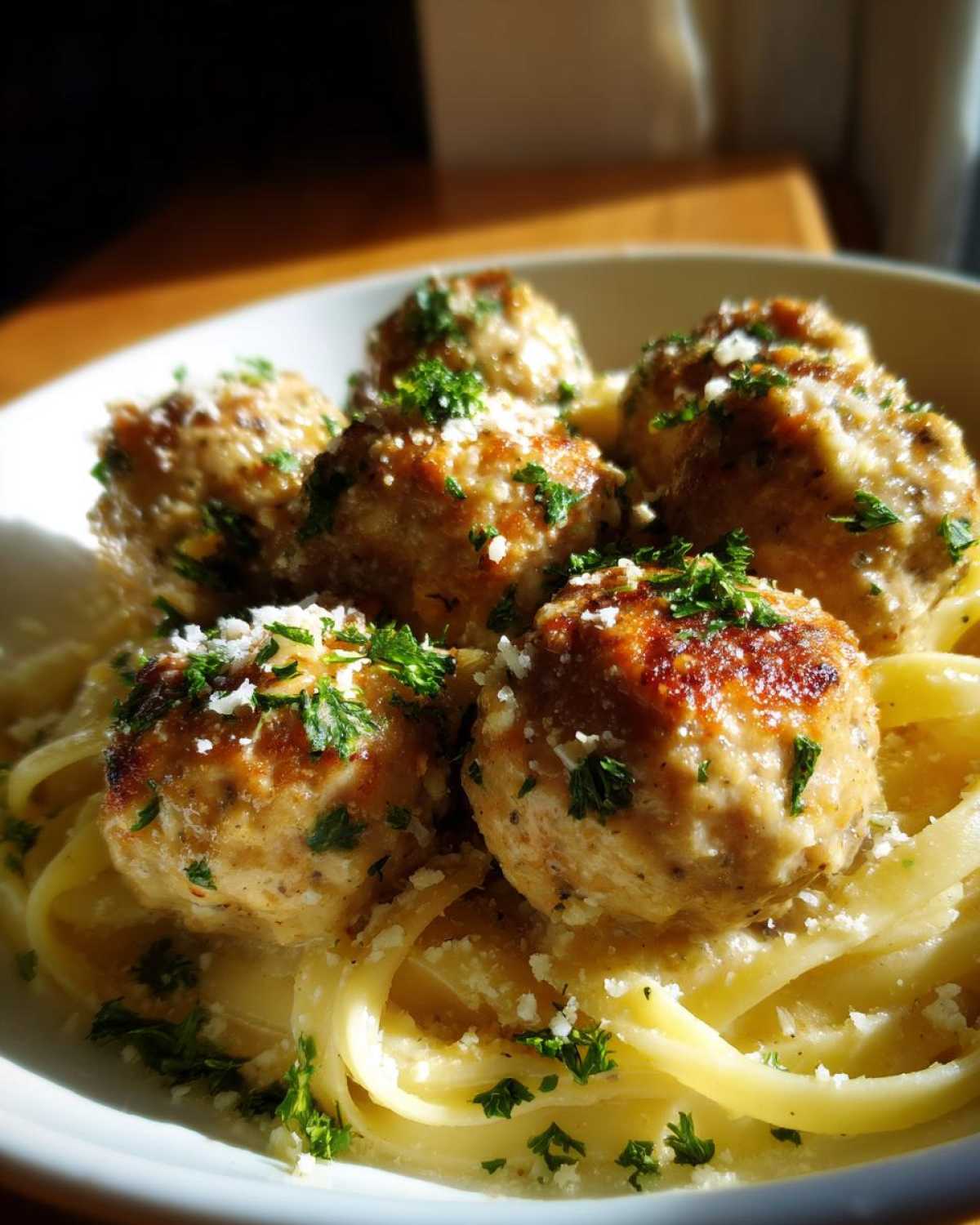 A close-up of tender garlic butter meatballs served over fettuccine pasta, garnished with fresh parsley and grated Parmesan cheese.