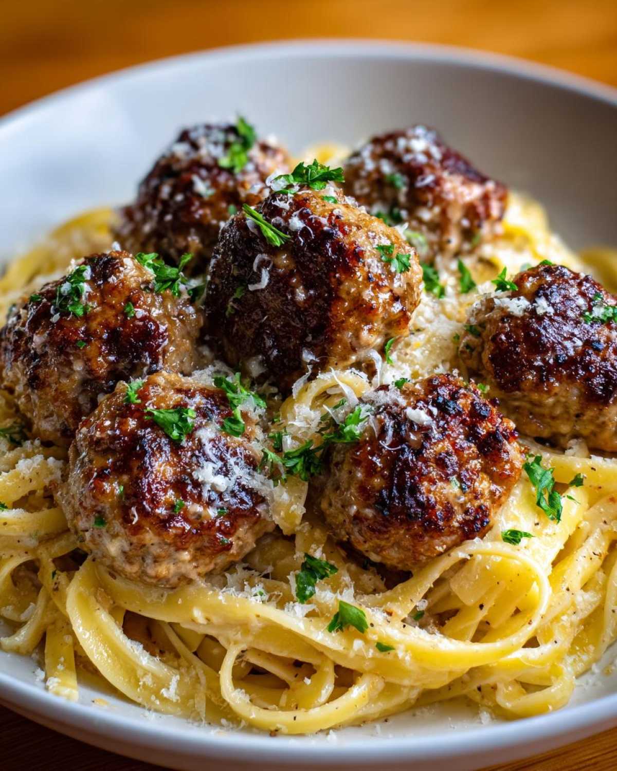 Close-up of juicy garlic butter meatballs served over creamy fettuccine pasta, garnished with parsley and Parmesan cheese.