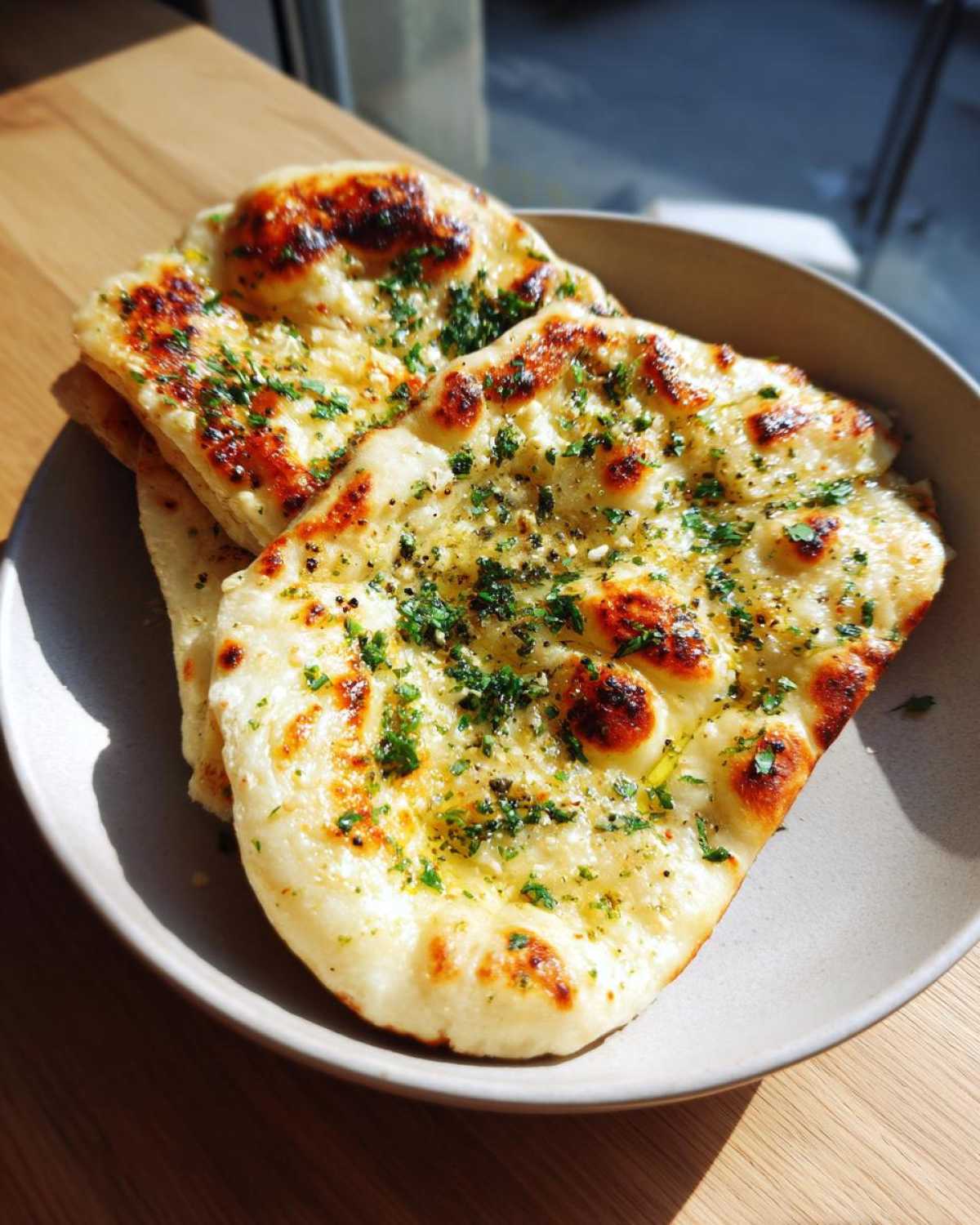 Close-up of two pieces of fluffy garlic naan bread topped with melted butter and fresh herbs.