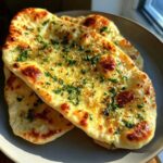 Close-up of fluffy garlic naan bread topped with melted butter, garlic, and fresh parsley, golden brown and slightly charred.