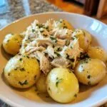 A bowl of shredded garlic parmesan crockpot chicken and potatoes, garnished with fresh parsley.