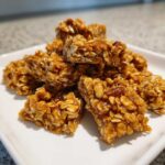 A pile of homemade granola clusters made with oats and a sticky binder, on a white plate.