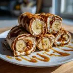 Close-up of stacked high protein banana roll-ups drizzled with caramel sauce on a white plate.