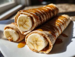 Three high protein banana roll-ups filled with peanut butter and banana, drizzled with caramel.