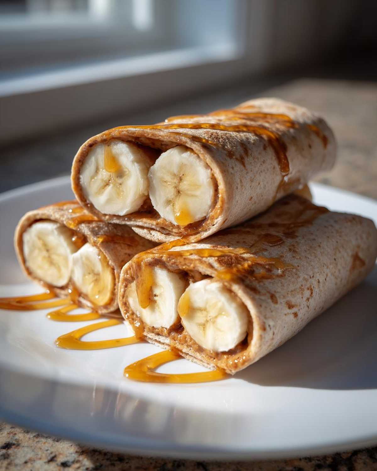 Three high protein banana roll-ups filled with peanut butter and banana slices, drizzled with honey.