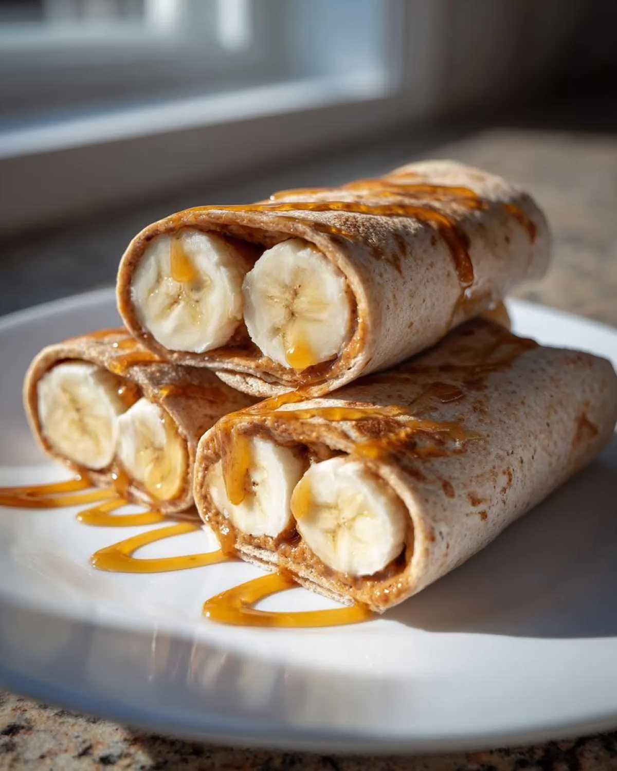 Three high protein banana roll-ups filled with peanut butter and banana slices, drizzled with honey.