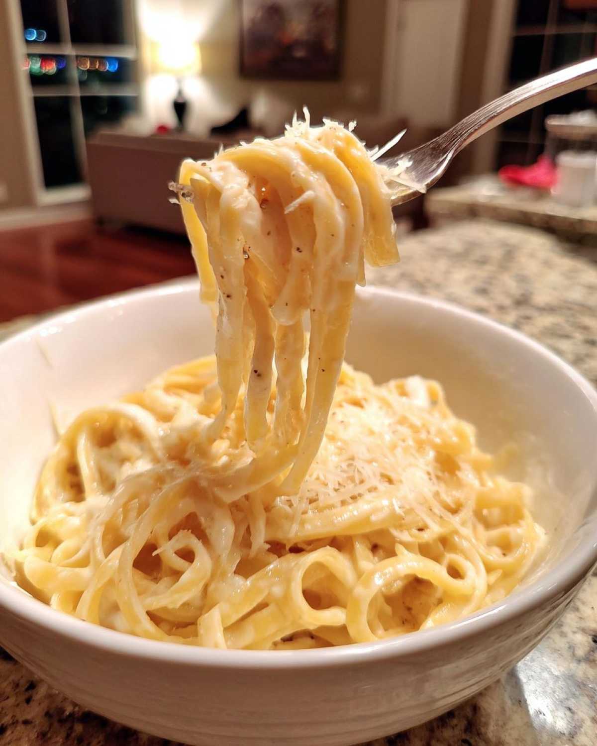 A fork lifting fettuccine pasta coated in creamy homemade alfredo sauce, sprinkled with Parmesan cheese.
