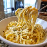 A fork lifting creamy fettuccine coated in homemade alfredo sauce, garnished with parsley and parmesan.